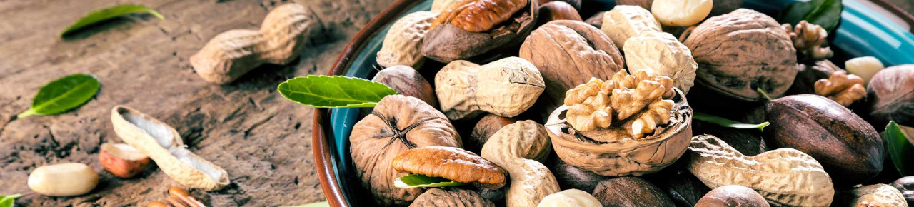 Verschiedene Nusssorten in einer blauen Schale, die auf hölzernen Untergrund steht