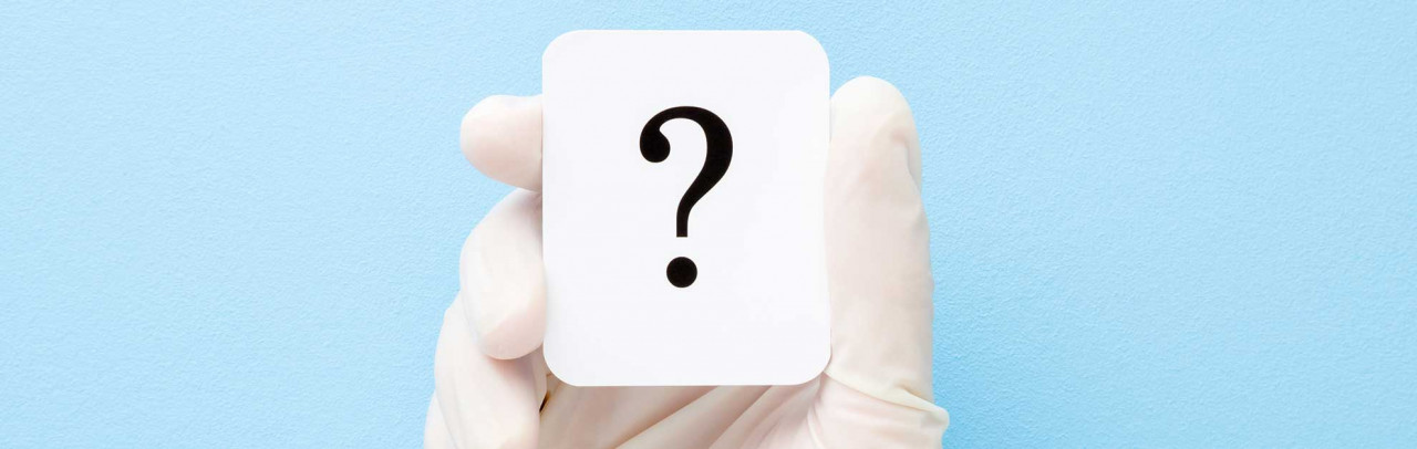 Hand in medizinischem Handschuh hält weiße Karte mit schwarzem Fragezeichen vor hellblauem Hintergrund