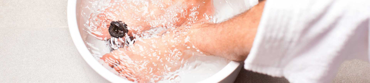 Ausschnitt eines Mannes in Bademantel, der seine Füße in einem Wasserbad wäscht