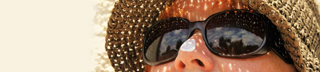 Frau mit Sonnenbrille und Sonnencreme auf der Nase