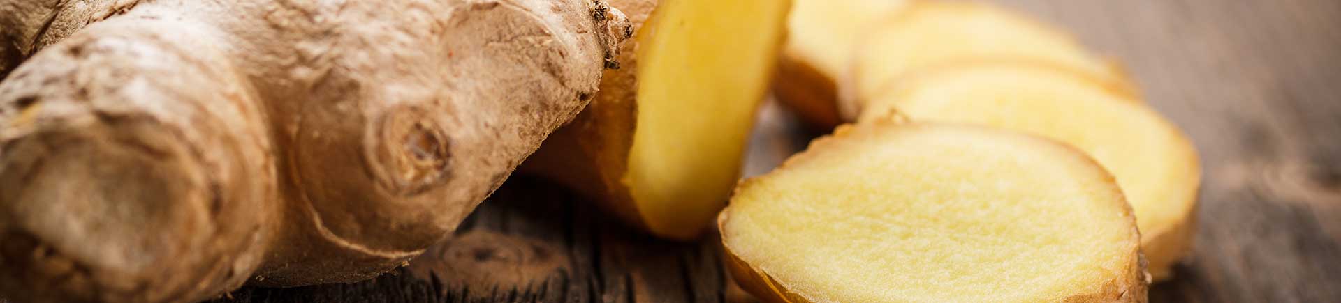 Eine Ingwer-Knolle in Scheiben geschnitten auf dunklem Holz